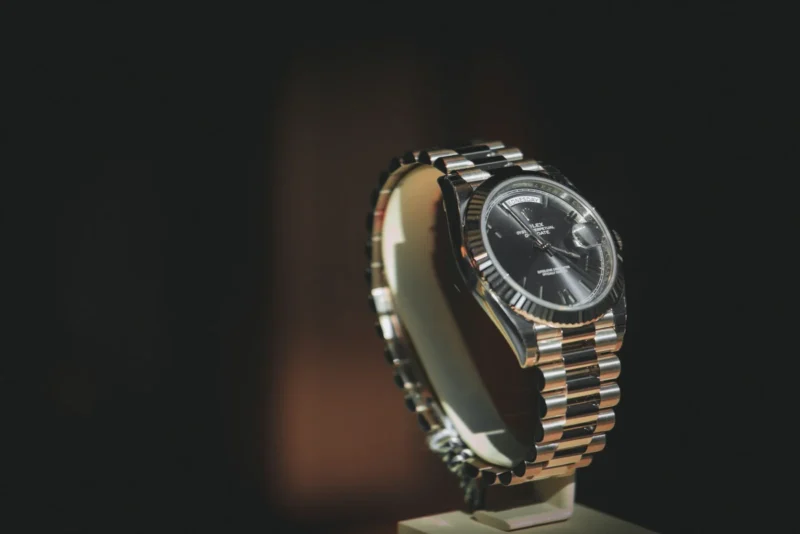 Rolex Day Date Oyster Perpetual watch with a black dial displayed on a stand against a dark background, illustrating how to spot a fake Rolex.