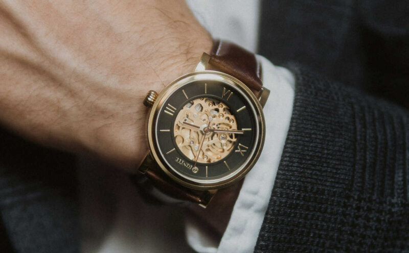 Close-up of a man's wrist wearing a second-hand luxury watch with a skeleton dial, Roman numerals, and a brown leather strap.