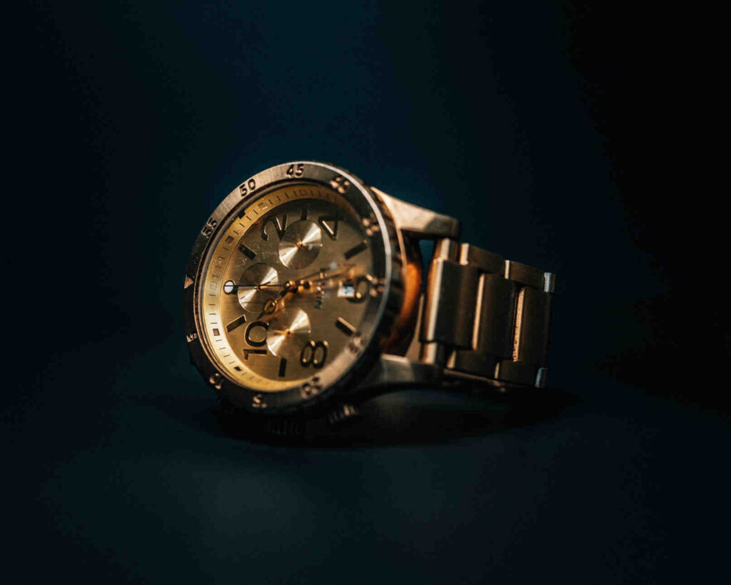 Gold volatility, close-up of a gold-toned chronograph watch with a metal bracelet in moody low-light photography.