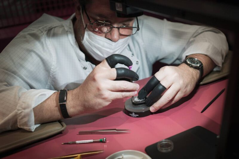 watchmaker performing luxury watch servicing and maintenance with precision tools at a workbench