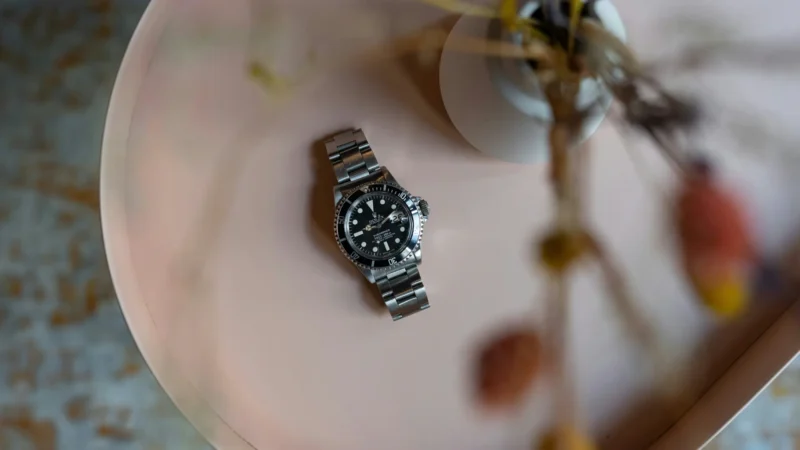Pre-owned Rolex Submariner steel watch resting on a pink surface, shown as the fastest-selling used luxury watch