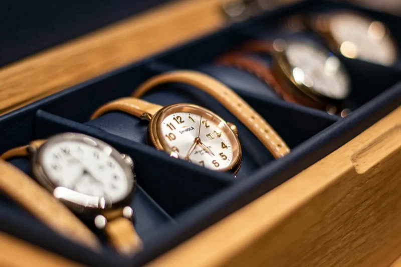 Wooden watch box with divided compartments holding several luxury watches including a Shinola, illustrating a watch consignment service.