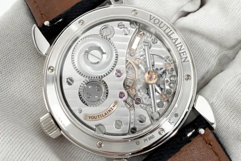 Close up of the exposed mechanical movement on the back of a Voutilainen watch, resting on a cloth with its brown leather strap visible.