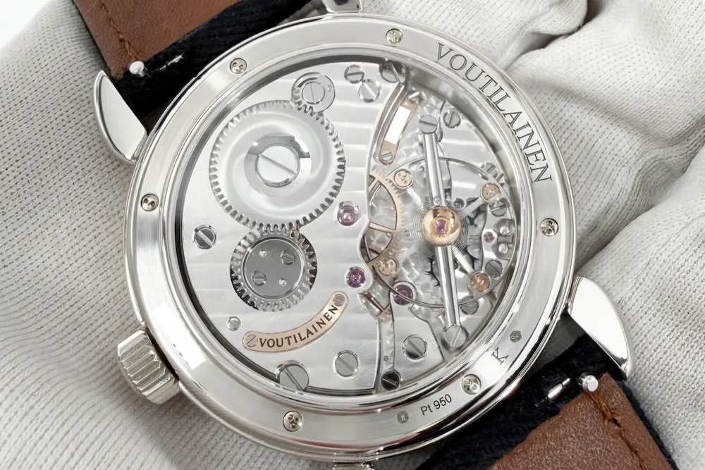 Close up of the exposed mechanical movement on the back of a Voutilainen watch, resting on a cloth with its brown leather strap visible.